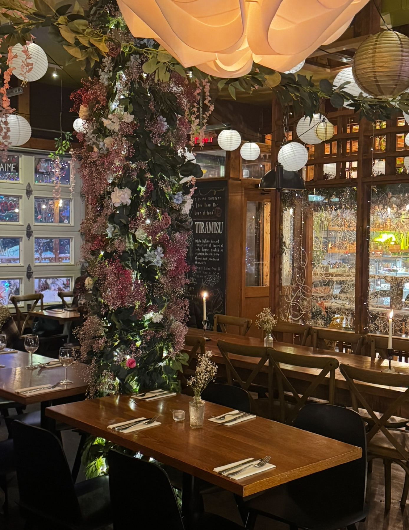 Tiramisu Bistro dining room with a floral pillar covered in hanging flowers, paper lanterns overhead, and the daily blackboard menu